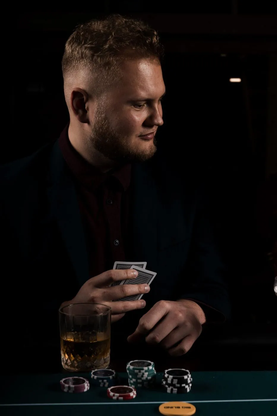 Gracz przy stole pokerowym z kartami i szklanką whisky